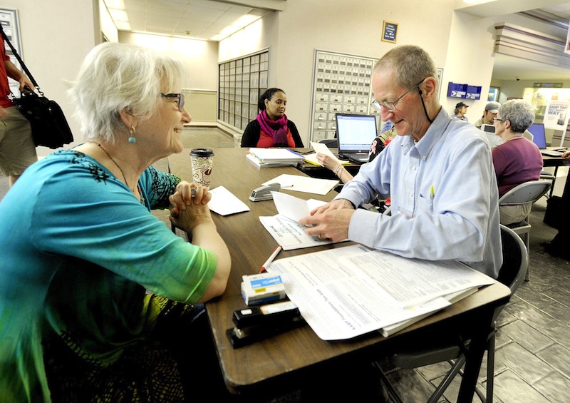 In this 2012 file photo, RJ Harper (right), an IRS certified volunteer tax preparer, helps Ana Dana of South Portland at the Forest Avenue Post Office. Americans are getting bigger tax refunds in 2014, averaging more than $3,000 so far.