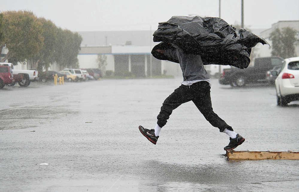 Worker Terry Young of Rialto, Calif., uses a sheet of plastic to protect himself from a downpour Friday as he jumps a flooded parking lot from a wood pallet to get to a food truck during his break in Anaheim, Calif.