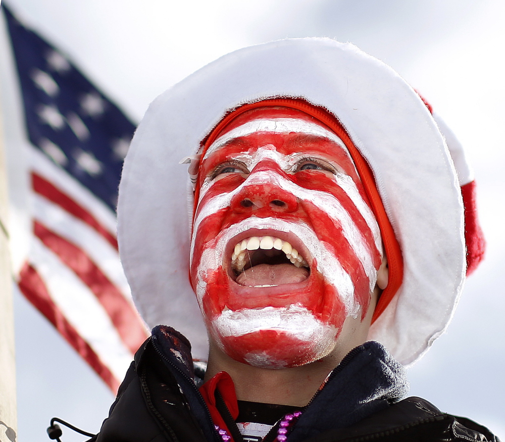 With his face painted and a large American flag in hand, Austin Huneck cheers for members of the U.S. biathlon team.