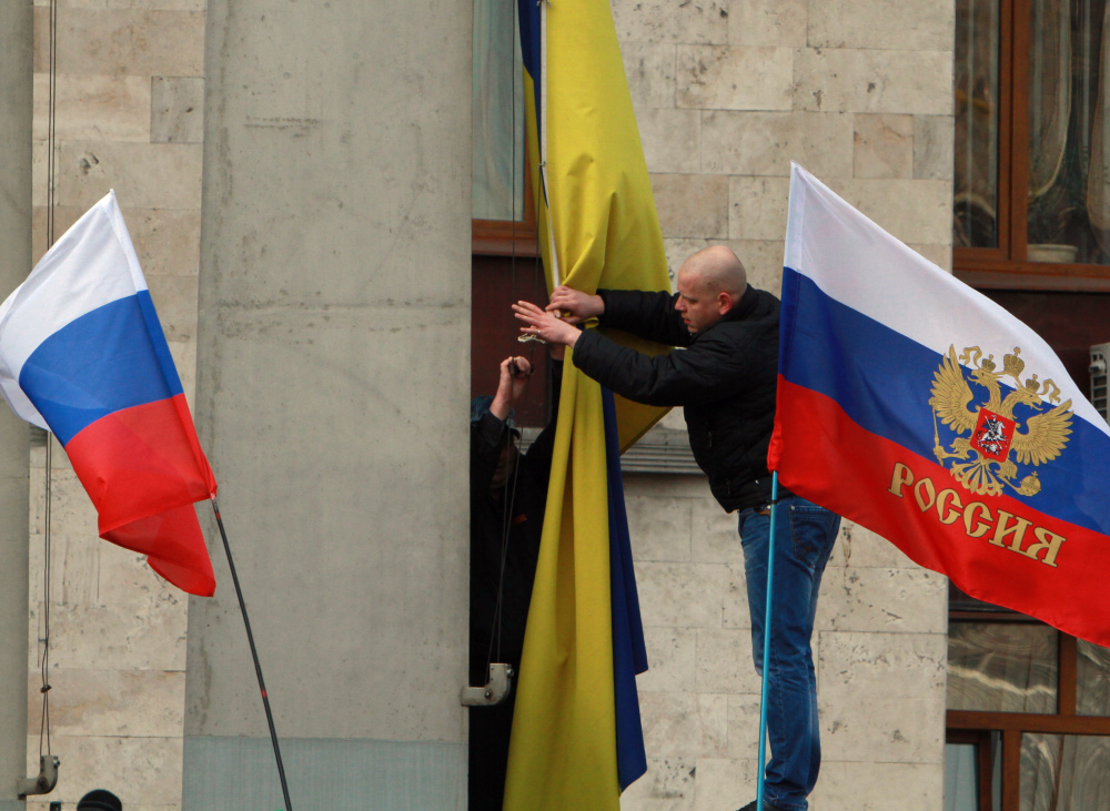Pro-Russian activists remove the Ukrainian flag, center, to replace it with a Russian one on an administration office in the center of Donetsk, Ukraine, on Saturday. Supporters of new Ukrainian authorities and pro-Russia demonstrators clashed in Kharkiv and Donetsk a mostly Russian-speaking region in eastern Ukraine.