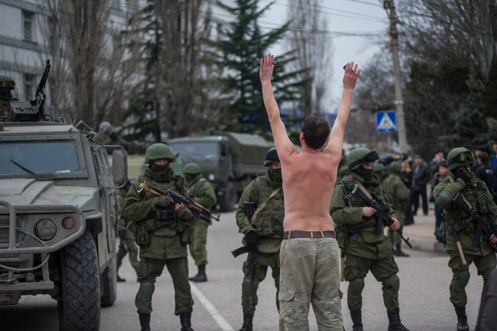 A Ukrainian man stands in protest in front of gunmen in unmarked uniforms as they stand guard in Balaklava, on the outskirts of Sevastopol, Ukraine, on Saturday. An emblem on one of the vehicles and their number plates identify them as belonging to the Russian military.