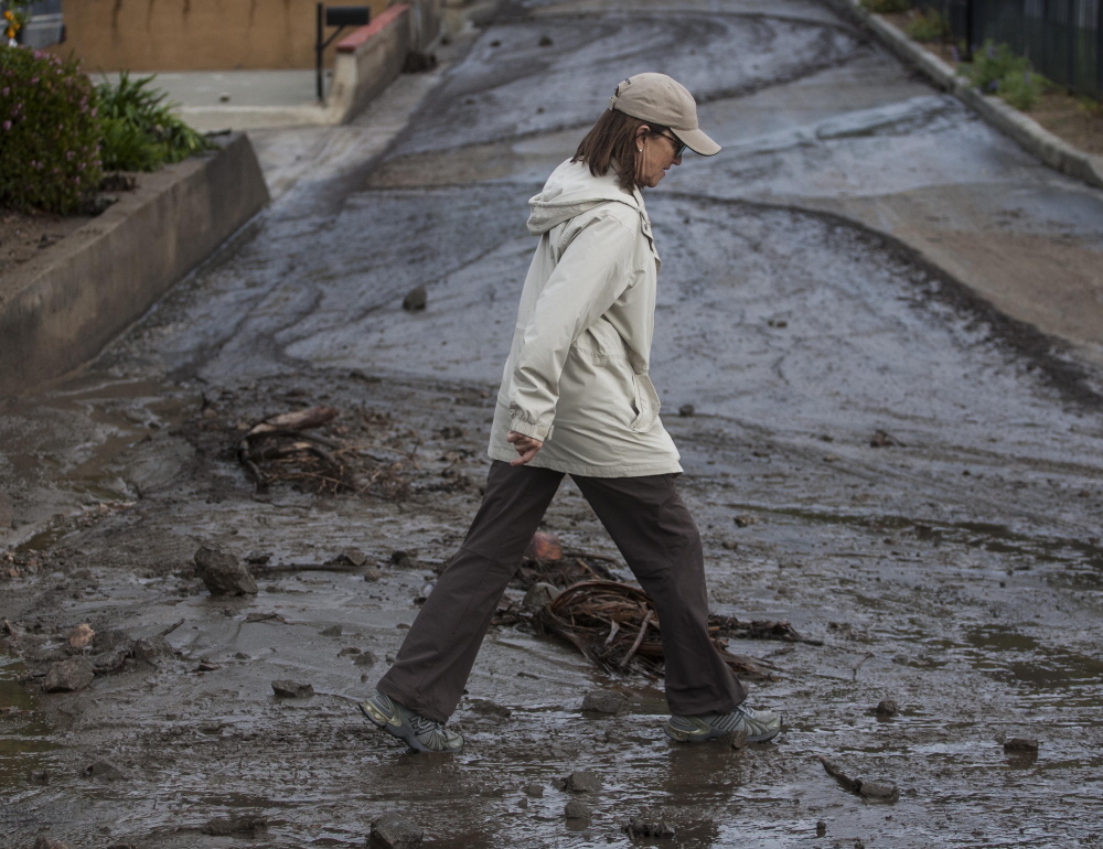 A woman walks over the mud and debris Saturday in Glendora, Calif. A burst of heavy showers before dawn caused another round of mud and debris flows in the city.