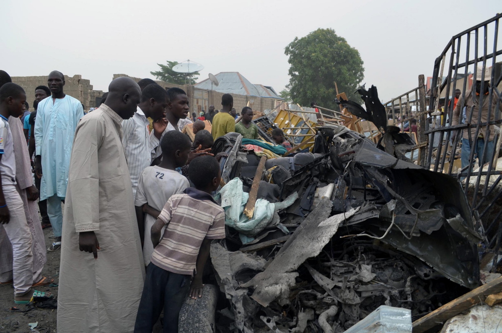 People gather to look at the remains of a car Sunday, after two car bombs exploded in Maiduguri, Nigeria, on Saturday night.