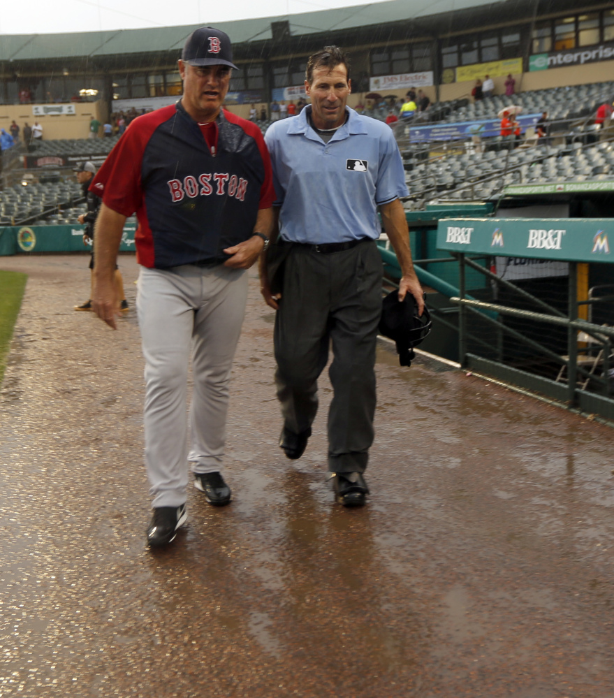 Boston Manager John Farrell and umpire Angel Hernandez leave the Jupiter, Fla., field after heavy rain in the eighth inning ends a scoreless exhibition game.