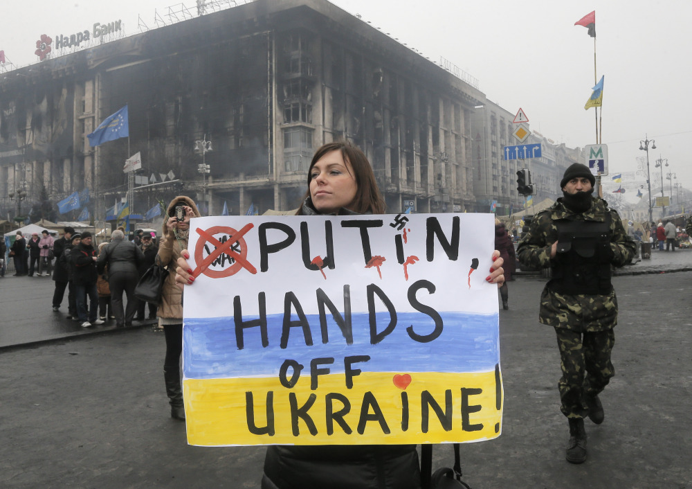 A woman holds a poster against war at Kiev’s Independence Square, in Ukraine, Thursday, March 6, 2014. The Heads of State of the EU will meet Thursday in emergency session in Brussels to discuss the situation in Ukraine. The destroyed trade union offices which was burned in clashes seen in the background.