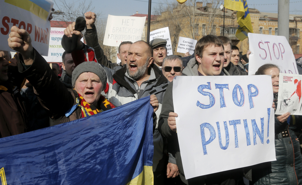 Demonstrators carry banners during a rally near the Russian embassy in Kiev, Ukraine, on Friday. As a result of its move into Ukraine, Russia already has lost billions from a stock market drop and the devaluation of the ruble.