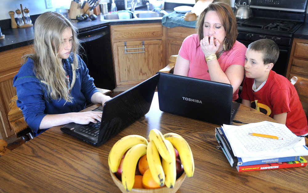 Kyrara Dawbin, 13, left, works on a lesson Thursday at the kitchen table with her mother, Karinna, and brother, Peter, 9, at their West Gardiner home. The Dawbins may enroll their children in Maine Connections Academy if it opens this fall.