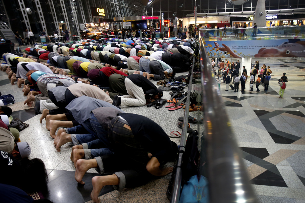Muslim men offer prayers at the Kuala Lumpur International Airport for the missing Malaysia Airlines jetliner MH370 on Thusday, while on a level down, travelers queue up at immigration checkpoints.