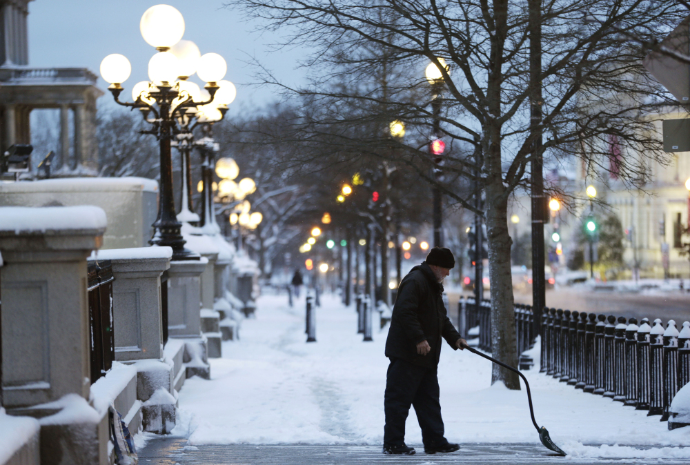 A man clears the sidewalk near the Eisenhower Executive Office Building on the White House complex in Washington, Monday, March 17, 2014, after an overnight snow hit the metro area, prompting area schools the federal and local government to close.