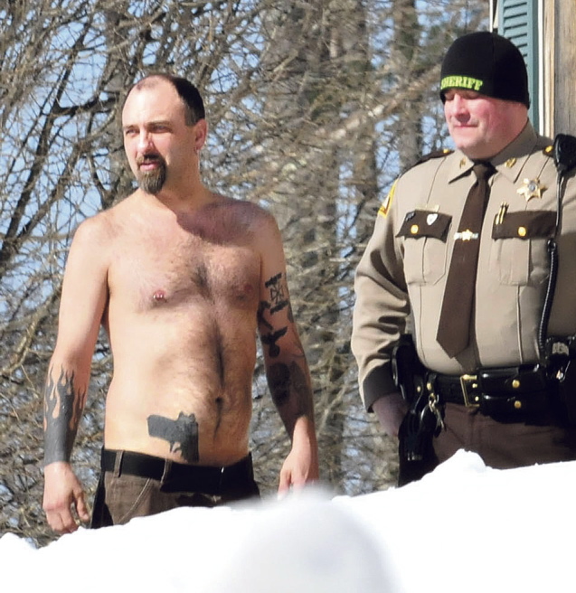 Norridgewock resident Michael Smith, with a tattoo of a gun at his waistband, stands beside a Somerset County sheriff’s deputy Tuesday morning.