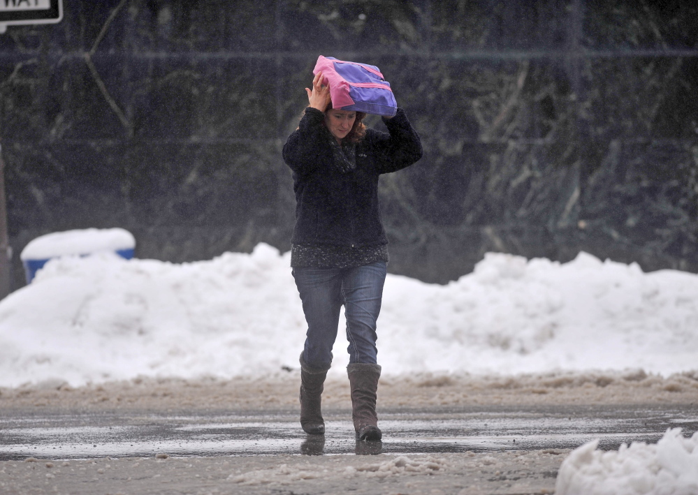 SPRING STORM: A pedestrian covers her head with a bag as she crosses Main Street in Waterville on Thursday.
