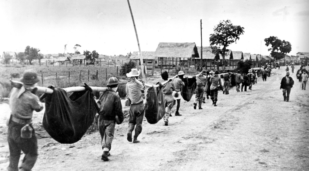 Allied prisoners of war carry their comrades in slings during a burial detail. In 2009, John E. Love, a Bataan Death March survivor, joined a campaign with other Bataan Death March survivors to change the caption of this photo.