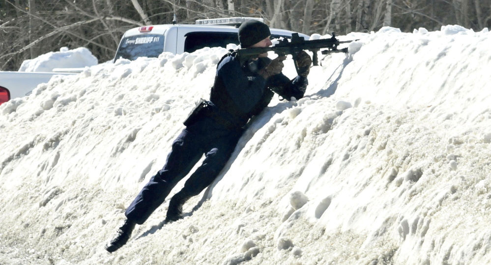 Maine State Police Trooper Scott Duff aims his rifle toward the home of Michael Smith as other police called for him to come out of the house in Norridgewock on Tuesday. Tree workers called police after they exchanged words with Smith regarding cutting wood under power lines and mistook a pistol tattoo for a real firearm.