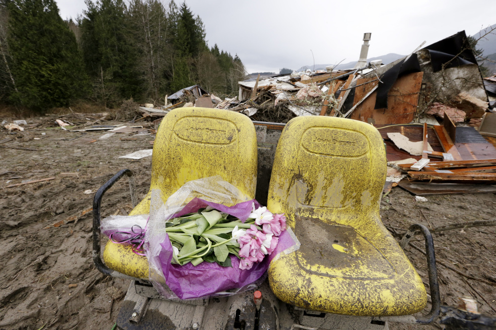 Flowers are left on debris Tuesday next to a demolished home where a woman’s body was found following a deadly mudslide in Arlington, Wash. At least 14 people were killed and searchers expect to find more bodies.