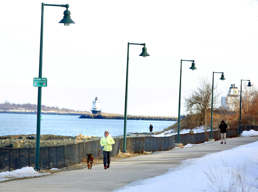 Christina Tavares of South Portland and her dog Hank run March 17 along the Eastern Promenade Trail. In the summer, there are guided tours of the lighthouse in the background, Spring Point Ledge Lighthouse in South Portland.