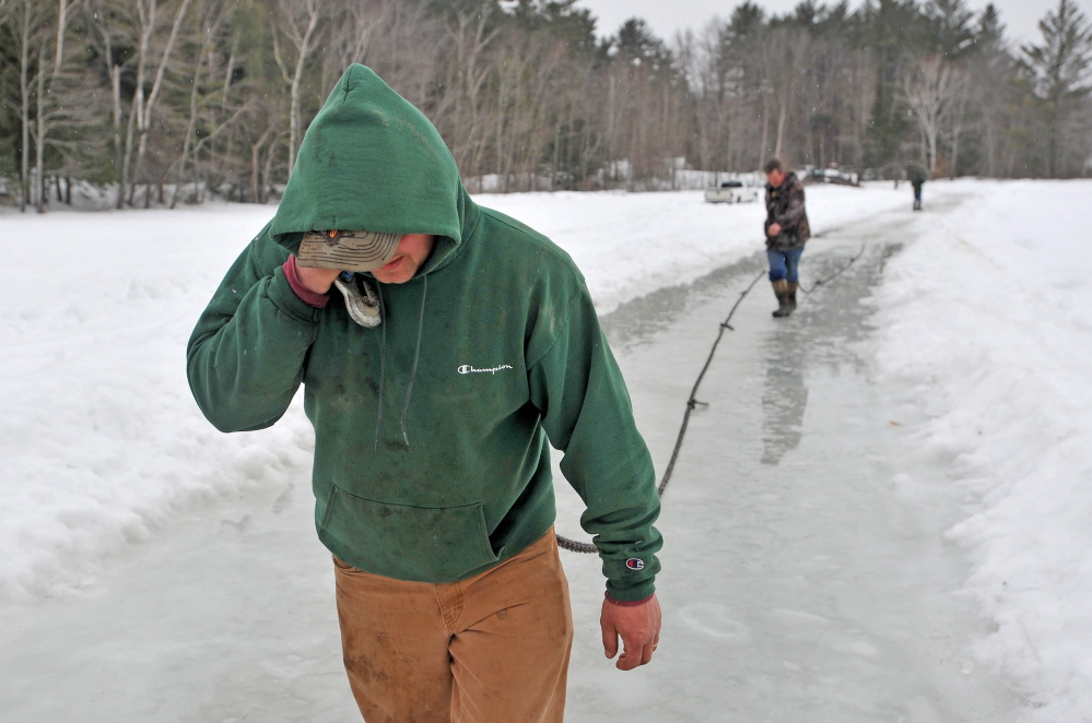 Steve Richardson, foreground, and Dave Richardson lay out nearly a quarter-mile of ropes and chains from Roger Hodgdon’s flatbed wrecker on Friday in a attempt to haul a stuck pickup truck, below, from the broken ice at Lake George in Canaan.