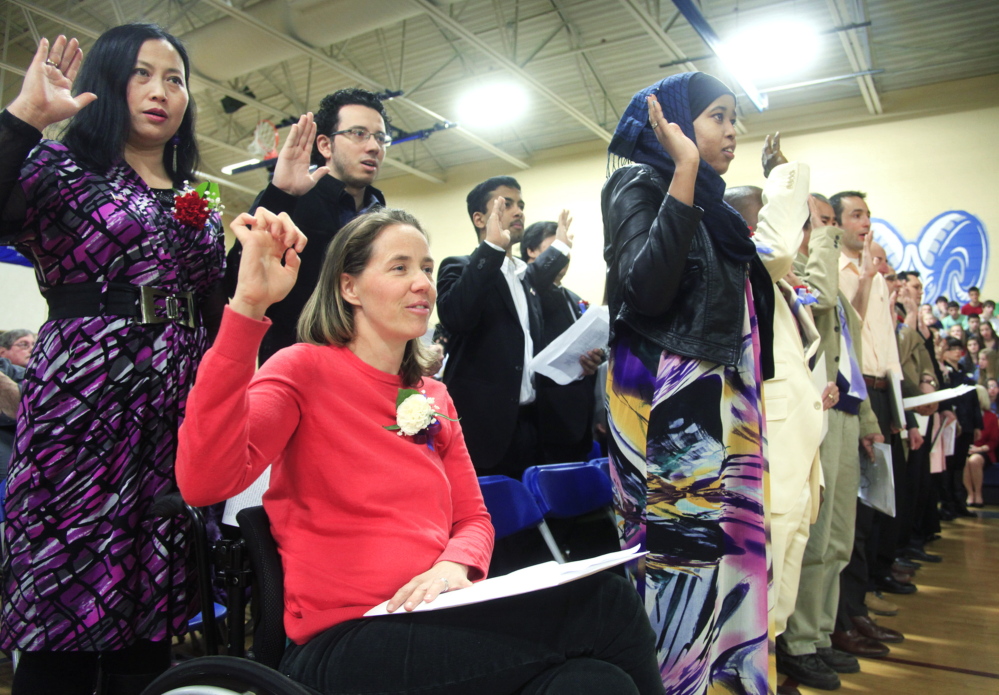 Beigette Gill of Harrison, in red, originally from Australia, joins other candidates for citizenship as they take the Oath of Allegiance during the U.S. Citizenship and Immigration Services naturalization ceremony at the Middle School of the Kennebunks in Kennebunk on Friday.