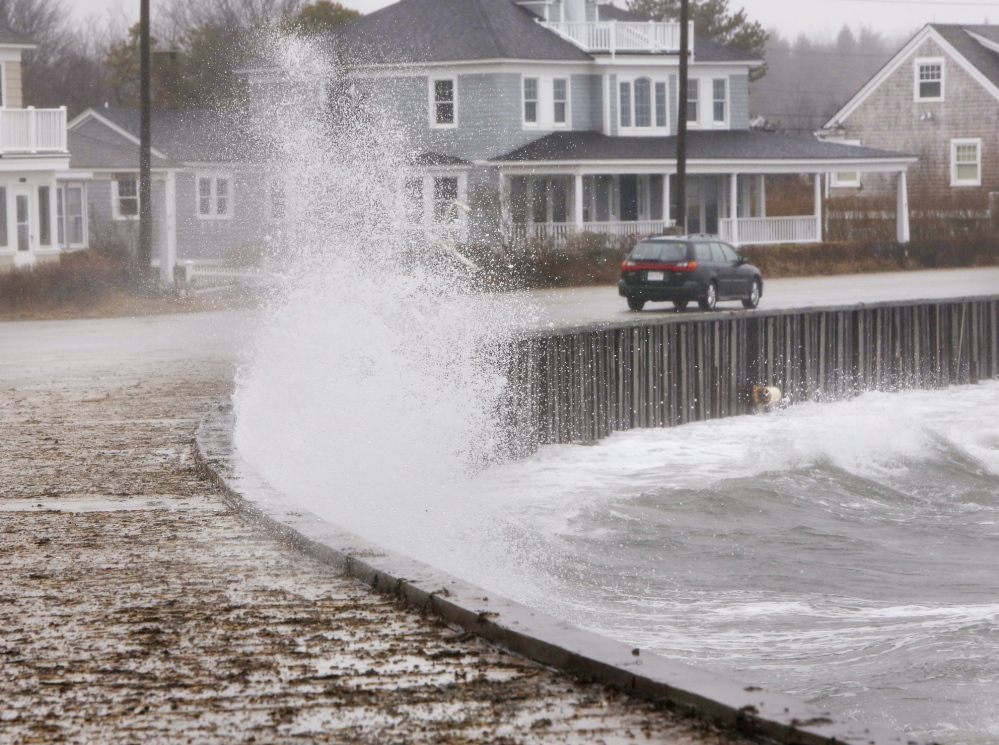 A car drives along Beach Avenue in Kennebunk on Sunday, as a wave hits a seawall, splashing water onto the sidewalk.