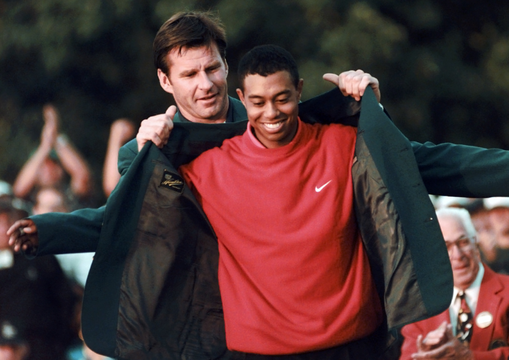 In this April 13, 1997, photo, Masters champion Tiger Woods receives his green jacket from the previous year’s winner, Nick Faldo, at the Augusta National Golf Club in Augusta, Ga.