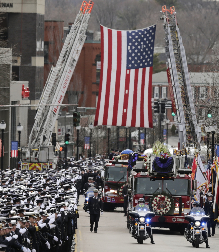 The funeral procession for Lt. Edward Walsh rolls under a flag spanning Main Street en route to St. Patrick’s Church in Watertown, Mass., Wednesday. Walsh and colleague Michael Kennedy died while battling a nine-alarm blaze in Boston’s Back Bay.