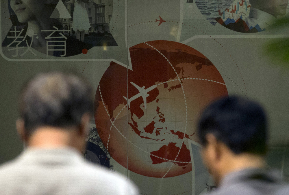 Relatives of Chinese passengers onboard the Malaysia Airlines flight MH370 walk past an advertisement for a bank depicting a plane flying over Asia at a hotel in Beijing Thursday, April 3, 2014. No trace of the Boeing 777 has been found nearly a month after it vanished in the early hours of March 8 on a flight from Kuala Lumpur to Beijing with 239 people on board.