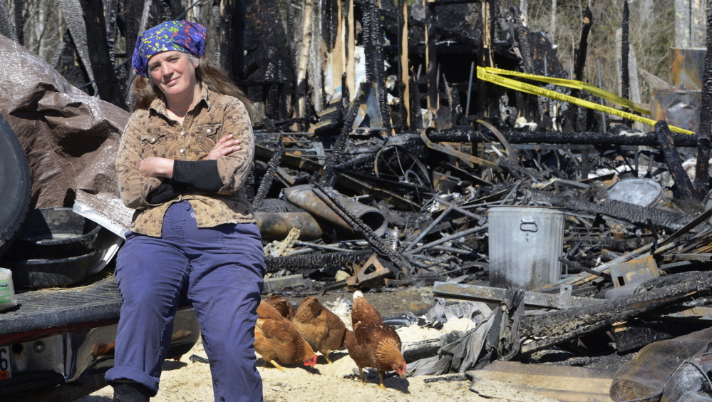 North Yarmouth farmer Jules Fecteau sits on the back of her truck against the backdrop of her barn that was destroyed by fire early Monday. The blaze was so destructive that the cause may never be determined for sure, a state fire investigator said Friday.