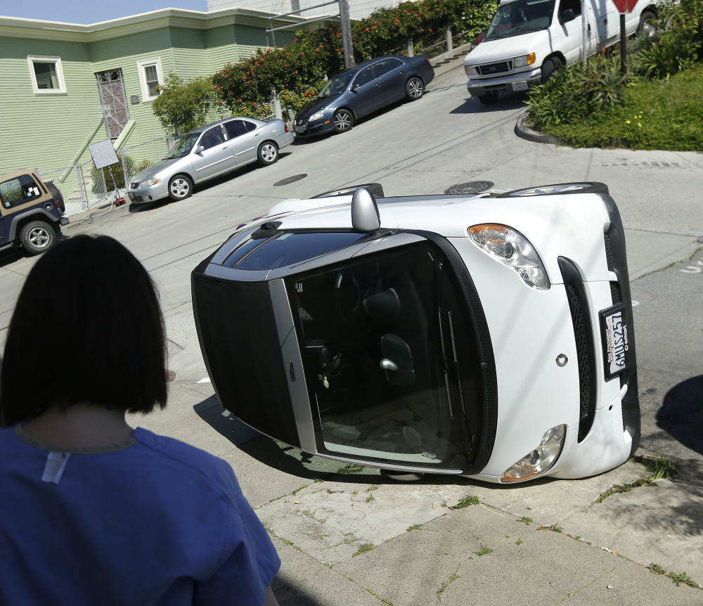 Shelley Gallivan looks toward a tipped-over Smart car in San Francisco. Police are investigating why four Smart cars were flipped over Monday during an apparent vandalism spree.