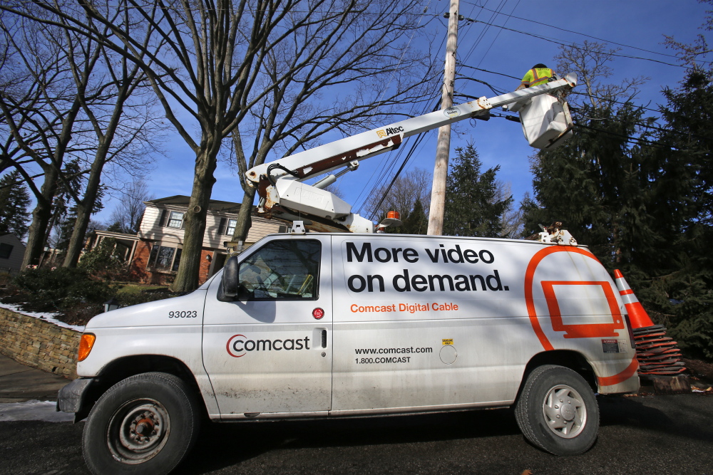 A Comcast cable truck works in front of a home in Mount Lebanon, Pa., recently. Comcast says it will provide its Internet Essentials program, offering Web access for $9.95 monthly to low-income families, in former Time Warner markets.