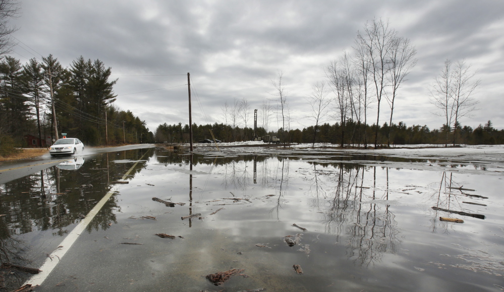 A car passes through a section of Route 113 in Standish that is covered by water near a low-lying field Tuesday.