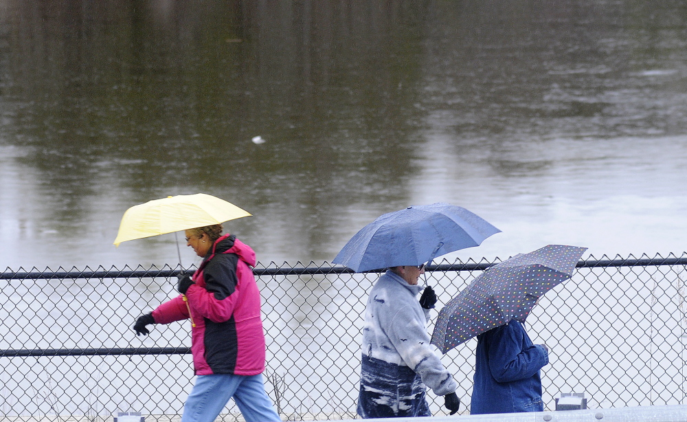 Walkers along the Kennebec River Rail Trail shelter themselves from rain Sunday from raindrops alongside the Kennebec River in Farmingdale. The National Weather Service issued a flood watch for Kennebec County through Wednesday as temperatures are expected to rise Monday with showers approaching Tuesday.