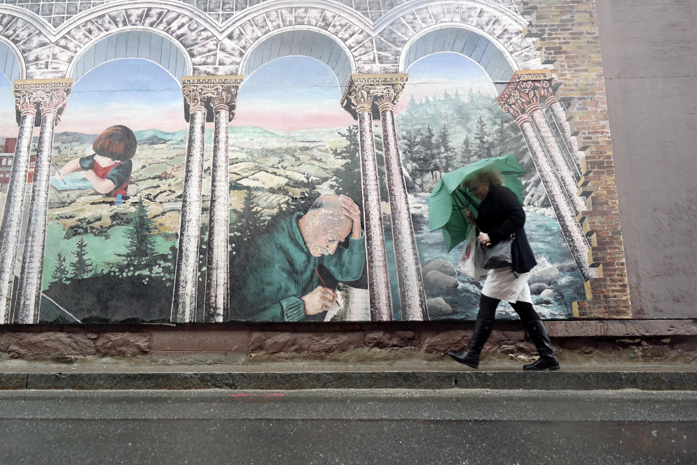 A woman takes shelter under her umbrella as she walks past a mural in Pittsfield, Mass., on Tuesday.