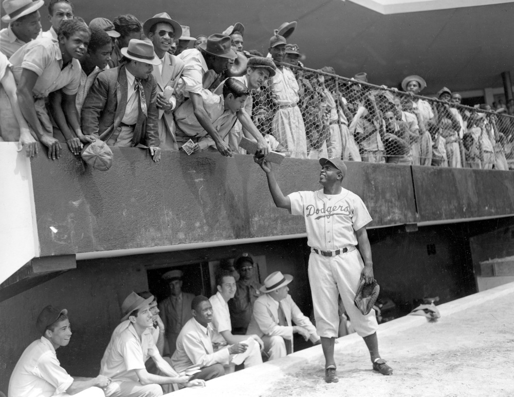 Jackie Robinson, first baseman of the Brooklyn Dodgers, returns an autograph book to a fan in the stands on March 6, 1948, during the Dodgers' spring training in Ciudad Trujillo, now Santo Domingo, in the Dominican Republic.