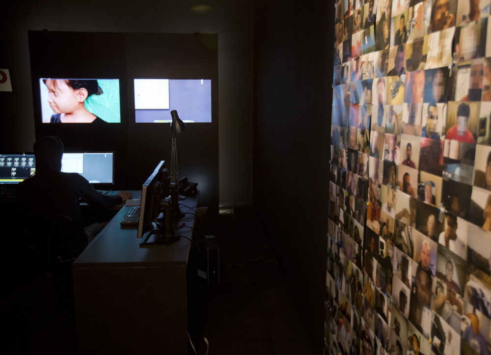 An investigator fishes for pedophilia suspects near a wall plastered with pictures of men who have sought out Sweetie, a computer generated image, at left.