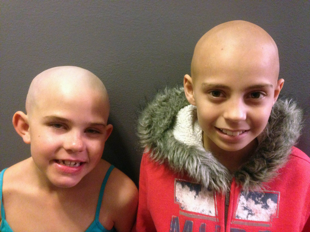 Kamryn Renfro, 9, left, and Delaney Clements, 11, right, stand together for a photo last month in Grand Junction, Colo., shortly after Kamryn had her head shaved to support Delaney, who lost her hair after treatment for cancer. Kamryn was suspended from her public charter school in Grand Junction because a shaved head goes against the school’s dress code. But the school quickly reversed the decision.