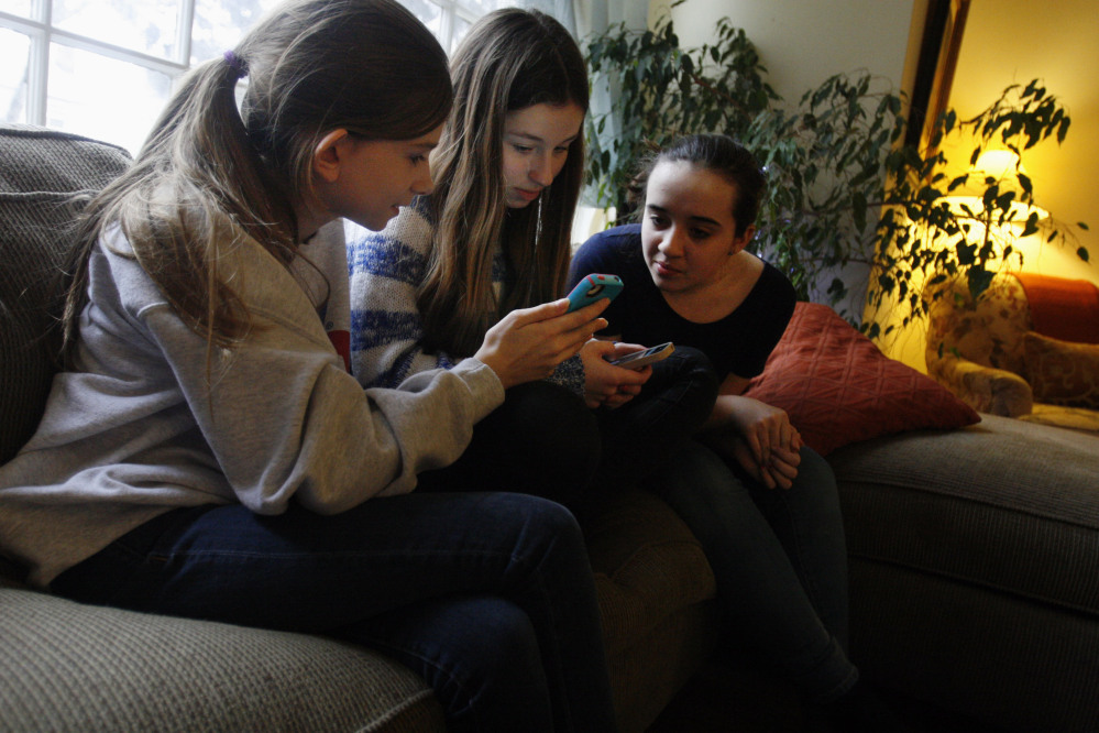 Kate McClintock, 12, left, Kate Green, 13, and Lilly Bond, 13, look at their smartphones at Lilly’s home in Evanston, Ill., last week. The friends are seventh-graders at Haven Middle School in Evanston, which has been at the center of a controversy over its dress code.