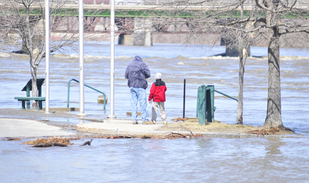 An adult and child watch the rising Kennebec River beside the Augusta Waterfront Park sign on Wednesday in downtown Augusta. The river was predicted to rise another few feet in the evening.
