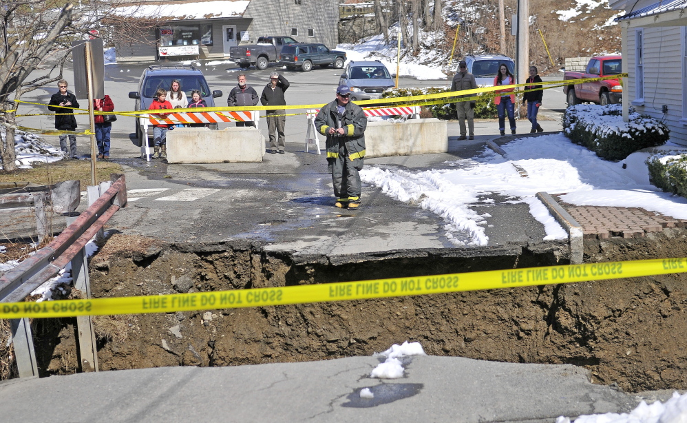 A firefighter stands at the edge of the washed-out connector street between Main and Water streets Wednesday in downtown Dexter.