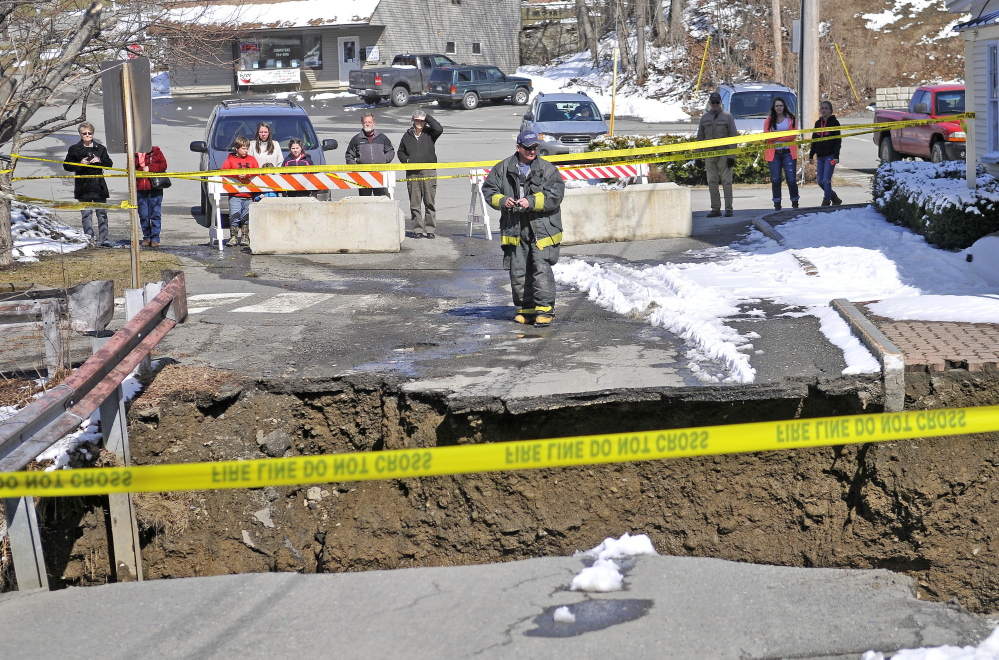 A firefighter stands by the edge of the washed-out connector street between Main Street and Water Street in downtown Dexter on Wednesday. Town Manager Shelley Watson said the town was still assessing flood damages.