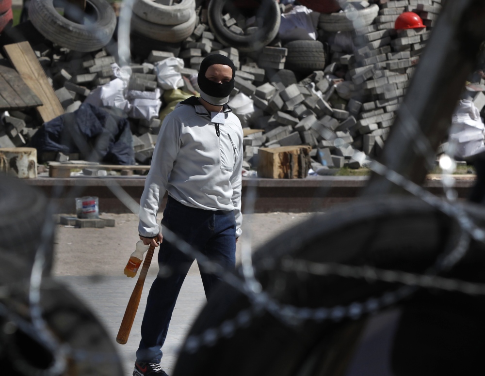 A masked activist walks among barricades Friday at an occupied building in Donetsk, Ukraine. Militants are calling for the interim government in Kiev to resign.