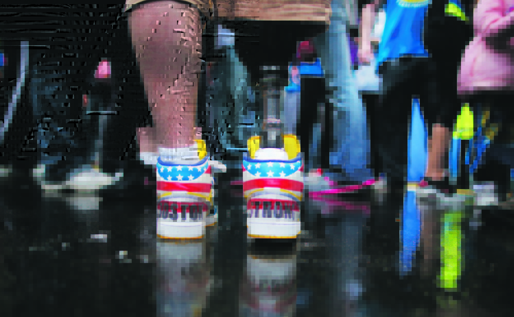 The shoes of 2013 Boston Marathon bombing survivor J.P. Norden read “Boston Strong” as he stands at the finish line on Tuesday, the one-year anniversary of the bombings. J.P. and his brother Paul, also a bombing survivor, took part in the final portion of the “Legs for Life Relay,” joining family members and friends who walked the entire marathon route to raise money for children needing prosthetic limbs.
