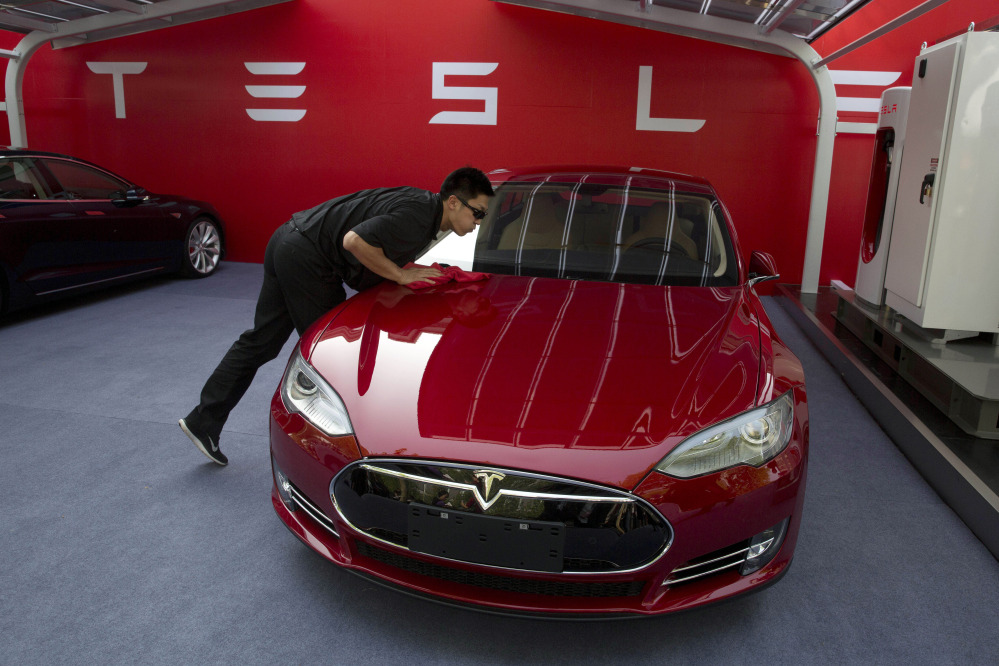 A worker cleans a Tesla Model S sedan before an event to deliver the first set of cars to customers in Beijing on Tuesday. CEO Elon Musk said the company will build a nationwide network of charging stations and service centers as fast as it can.