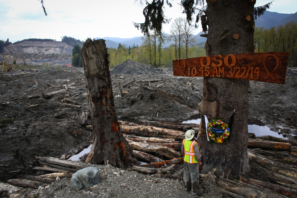 Ben Woodward looks up at a sign commemorating the moment of the Oso mudslide on Monday. The wooden memorial was attached to a towering spruce tree, one of the few in the debris field left standing after the disaster. Tuesday is the one month anniversary of the mudslide that killed a confirmed 41 people.