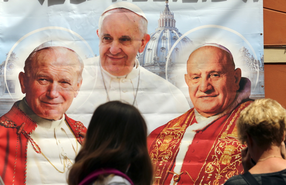 A woman takes a picture of an illustration depicting popes John Paul II, from left, Francis and John XXIII outside a shop in Rome on Thursday. Pope Francis will canonize John Paul II and John XXIII on Sunday.