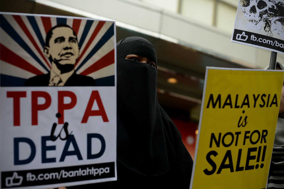 A Muslim woman, in Kuala Lumpur, Malaysia, on Saturday, holds placards during a protest against the Trans-Pacific Partnership in advance of President Obama’s visit. The president is taking two tracks in his words about China.