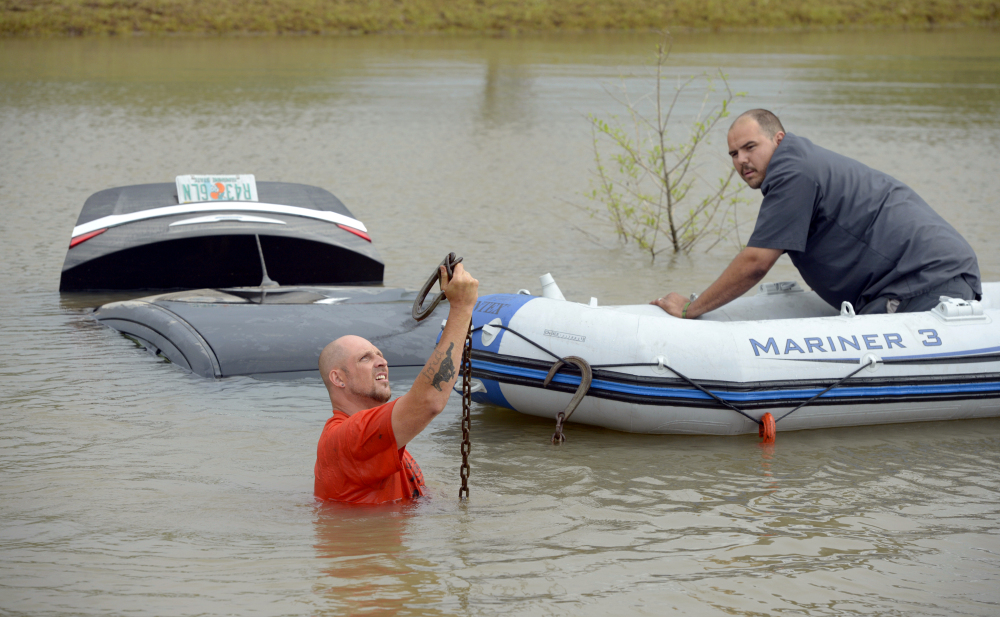 Michael Harrell, left, of J&J Towing holds up a tow cable before attaching it to a flooded car that was swept off Fairfield Avenue by torrential rains and deposited in a ditch as fellow employee Charles Thomas assists from an inflatable boat in Pensacola, Fla., on Wednesday.