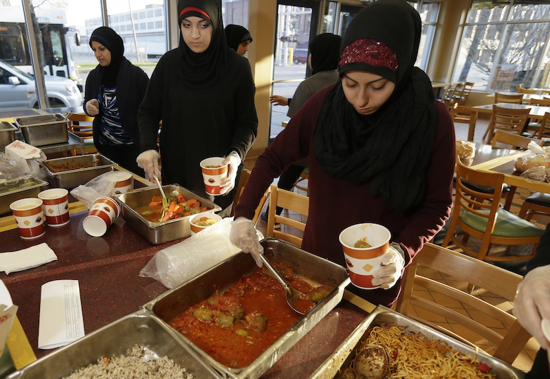 Volunteers Zahraa Debaja, center, and Zeinab Makki, right, prepare meals from food provided by the Yasmeen Bakery in Dearborn, Mich., Friday, April 25, 2014. The reach of one of the nation’s few charitable organizations exclusively providing halal food to the poor could be greatly expanded under the new federal provision.