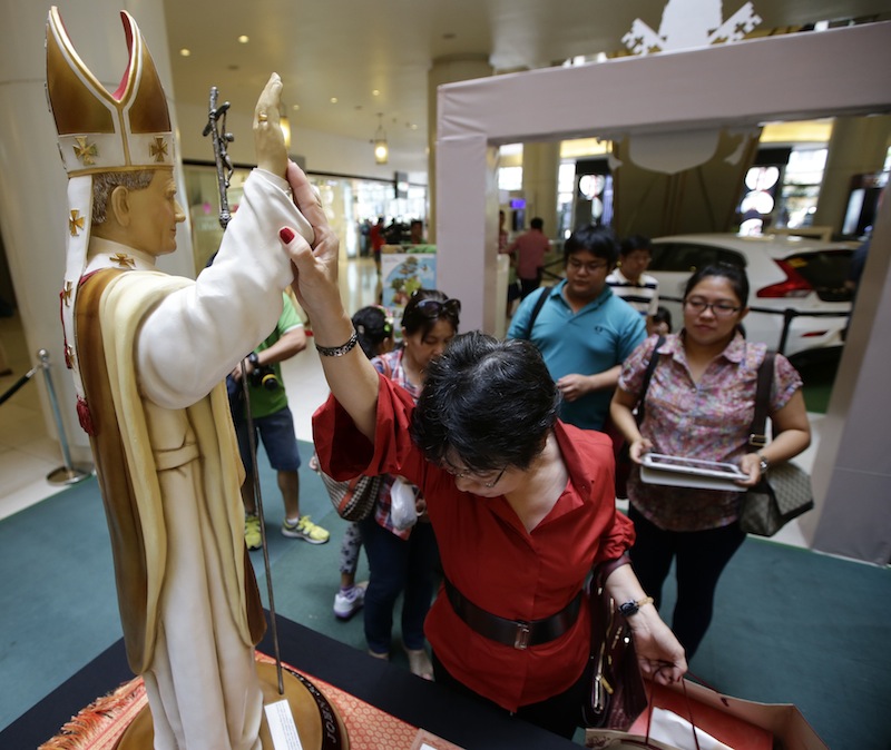 A devotee touches to pray at the statue of Roman Catholic Pope John Paul II on display with other relics of the late pope as well as Pope John XXIII in celebration of their canonization or the elevation to sainthood Sunday at suburban Quezon city, northeast of Manila, Philippines.