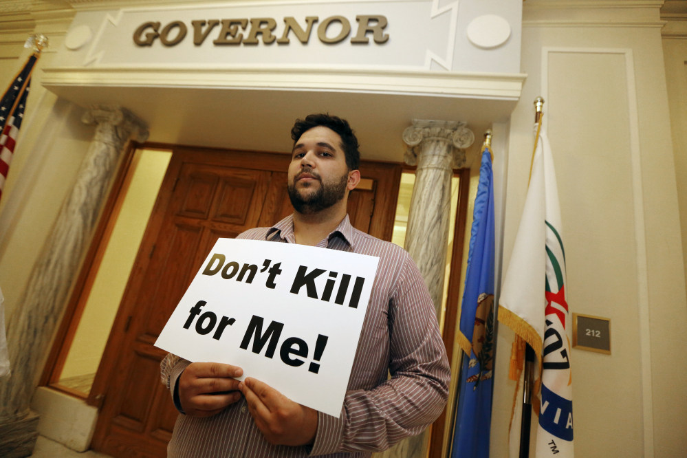 Hossein Dabiri with Oklahoma Coalition Against the Death Penalty holds a sign protesting the death penalty at the State Capitol in Oklahoma City on Tuesday. Oklahoma prison officials halted the execution of an inmate after the delivery of a new three-drug combination on Tuesday failed to go as planned.