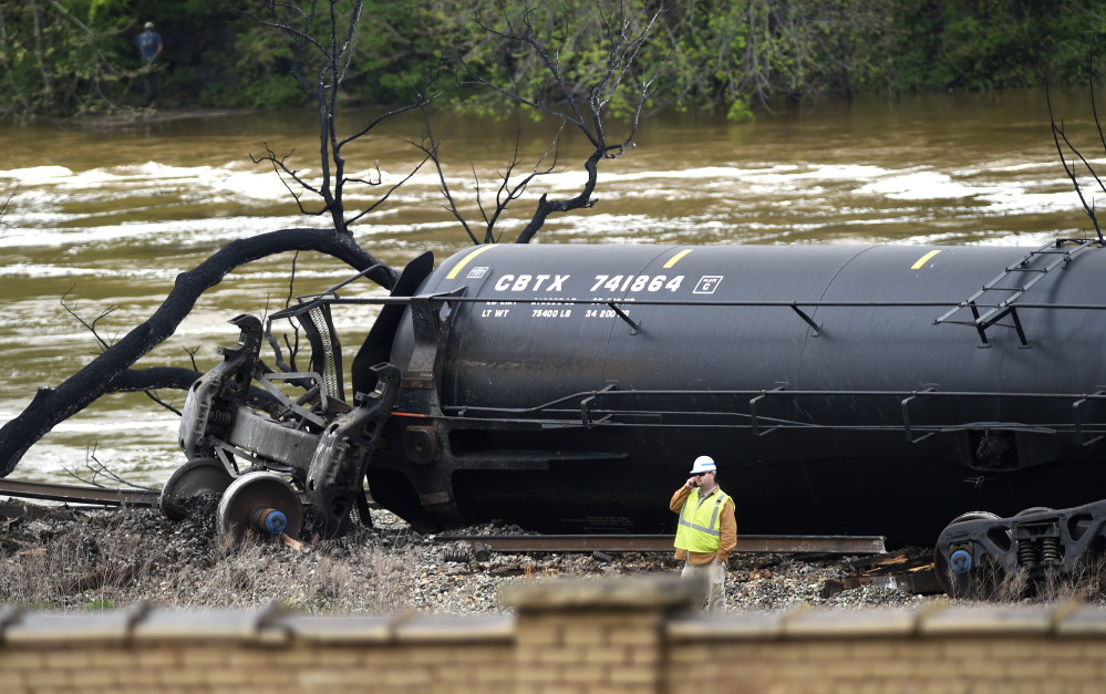 A worker stands Thursday by a damaged tanker car where several CSX cars carrying crude oil derailed and caught fire along the James River near downtown Lynchburg, Va.