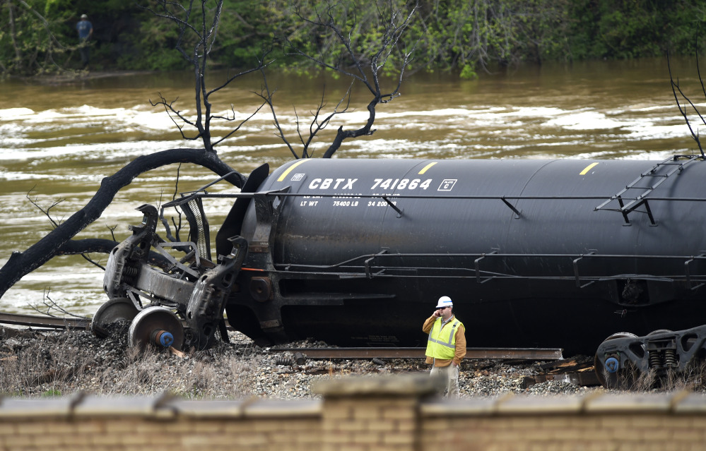 A worker stands on the bank of the James River near downtown Lynchburg, Va., on Thursday, beside a derailed and damaged tanker containing crude oil.